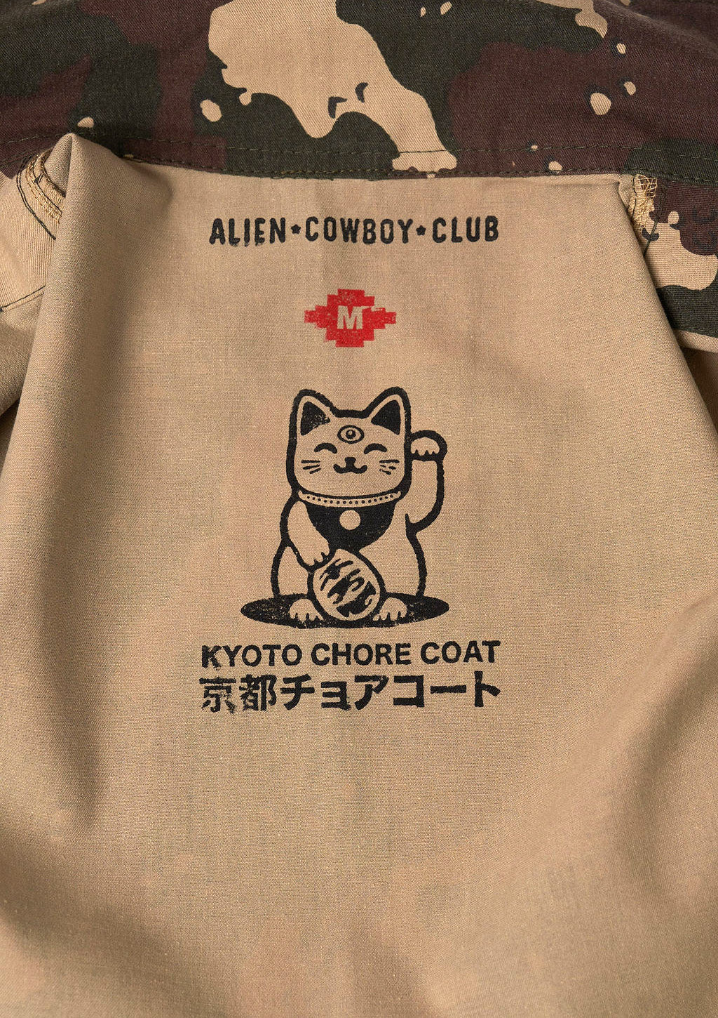 Beige coat with Alien Cowboy Club logo and cat illustration on a camouflage background